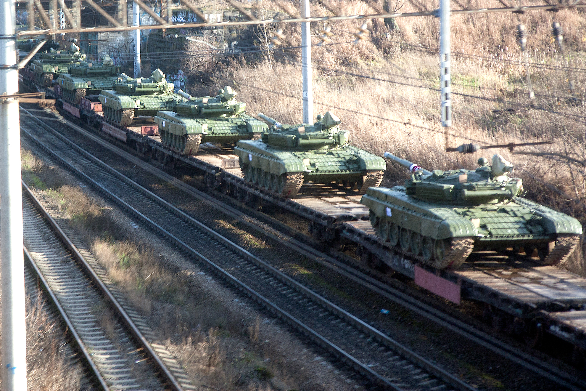 Tanks on the train being transporter through the middle of the city.